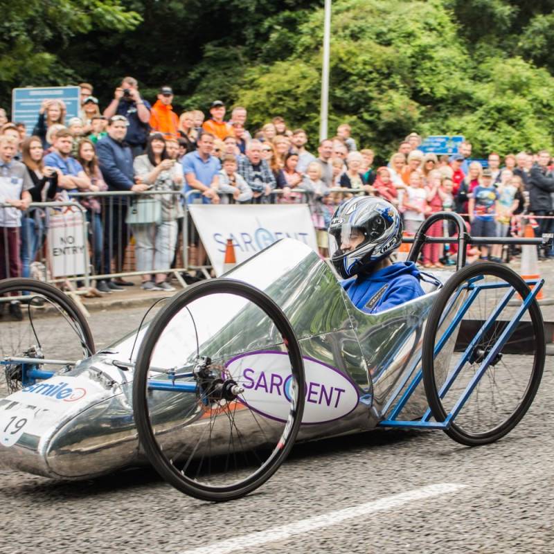 Sargent Electrical Soapbox going down a hill. Silver cart with big bike wheels.