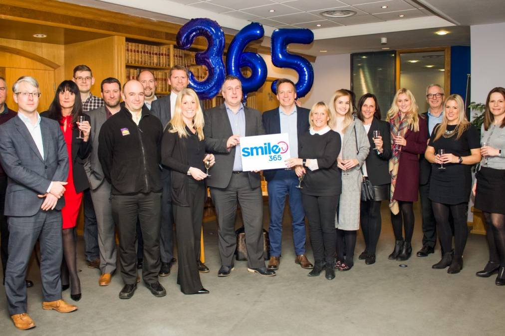 Smile365 Group of people with balloons in the background. Corporate setting.