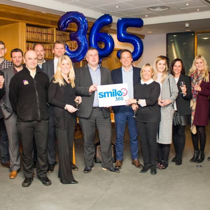 Smile365 Group of people with balloons in the background. Corporate setting.